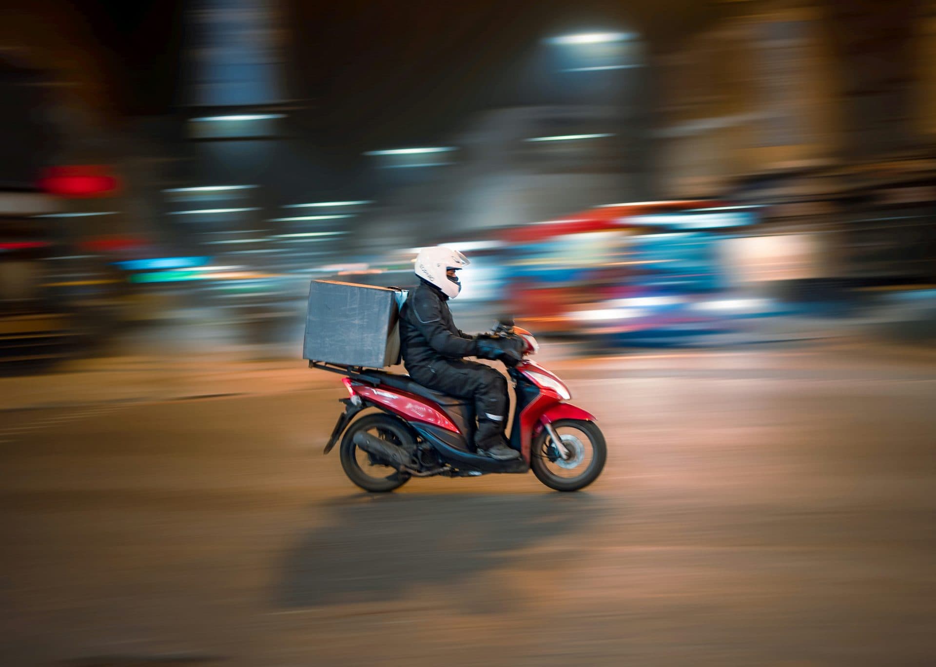 A delivery rider on a scooter moving through a city at night